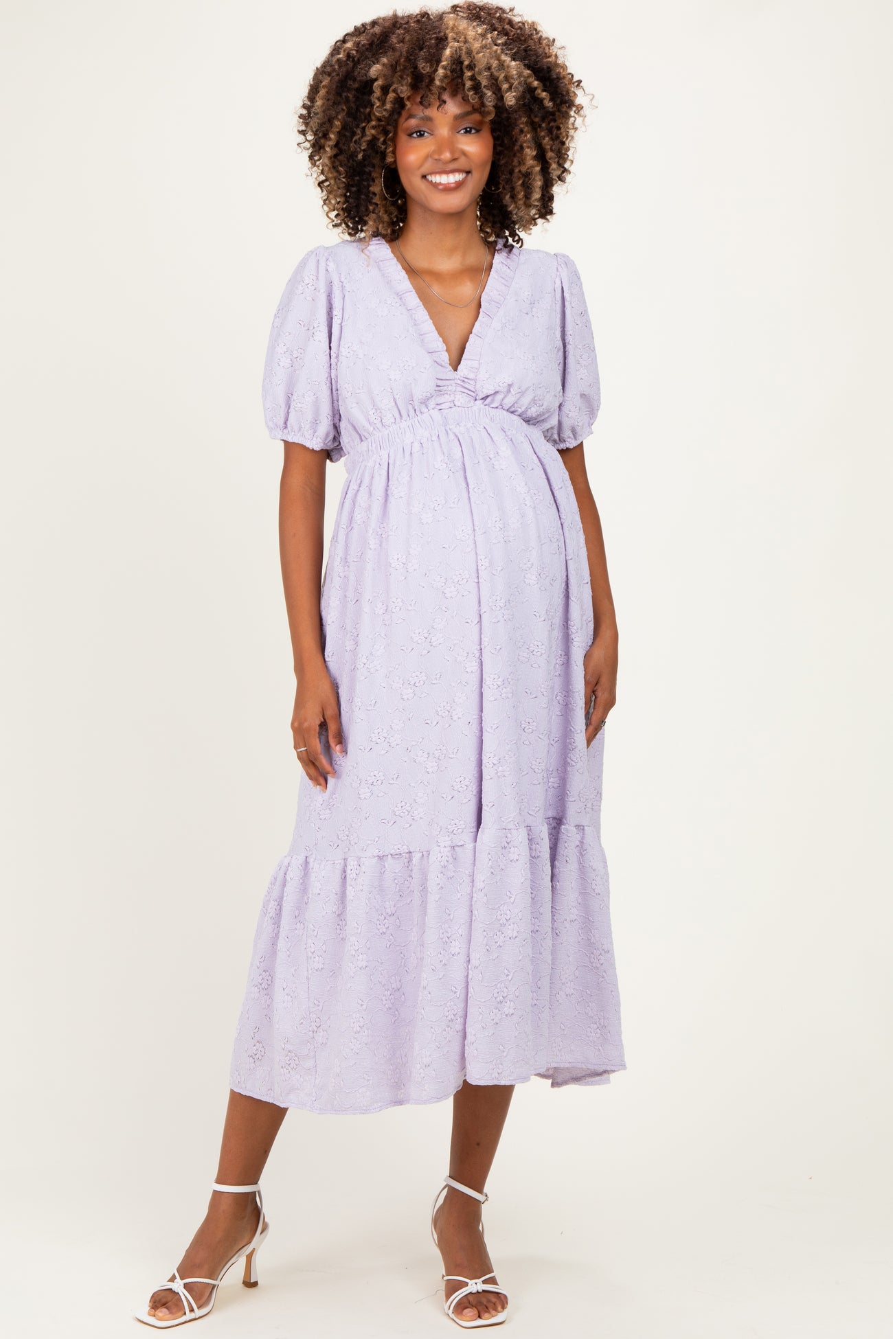 woman wearing a lavender maternity dress with puff sleeves and a tiered skirt, showcasing her baby bump