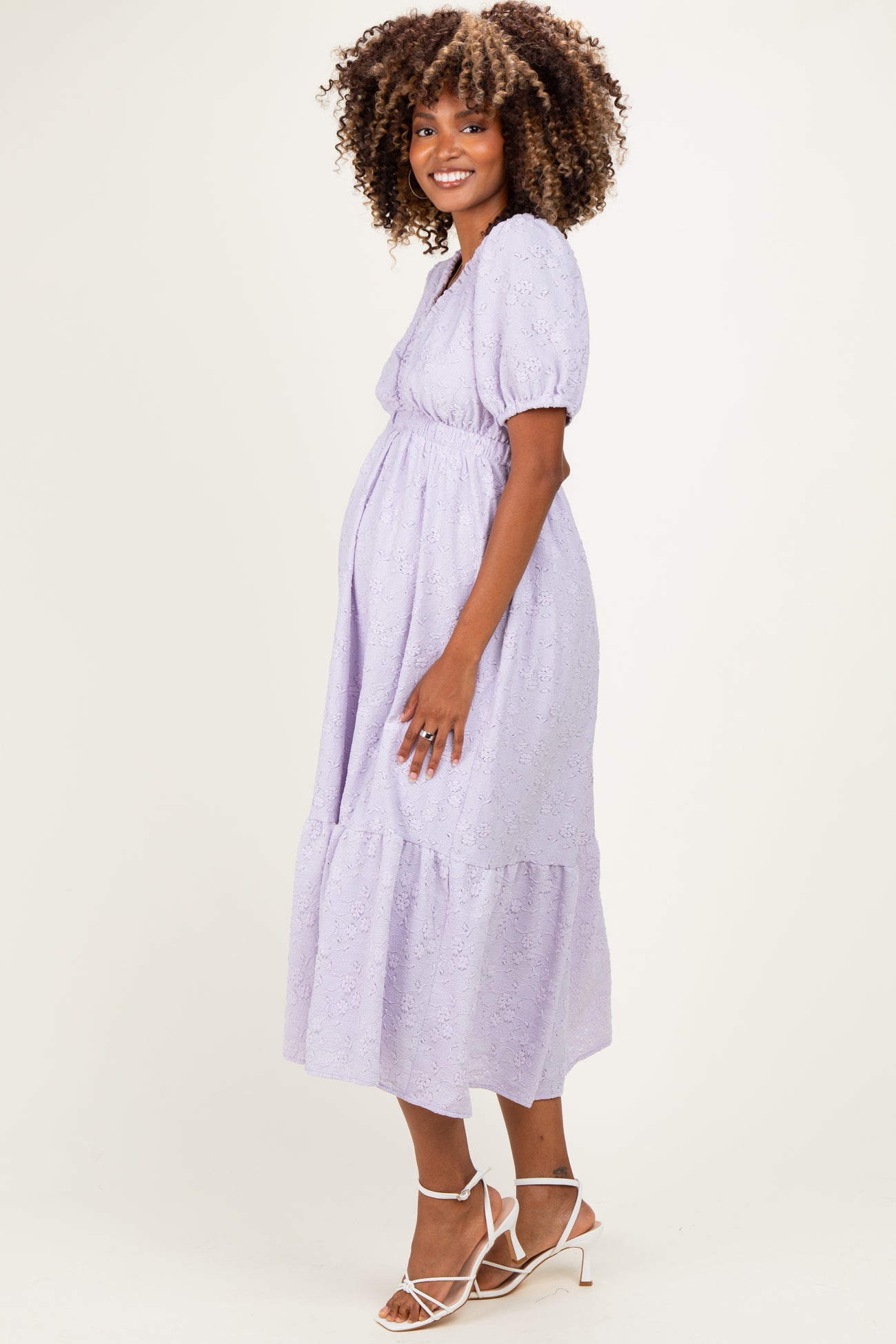 woman wearing a lavender maternity dress with puff sleeves and a tiered skirt, highlighting her baby bump