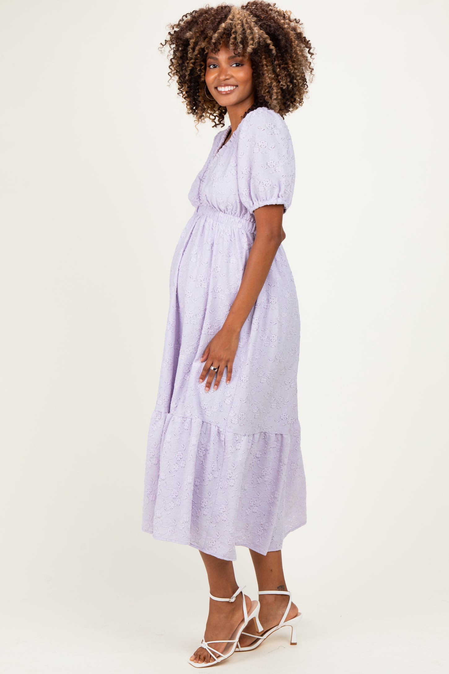 woman wearing a lavender maternity dress with puff sleeves and a tiered skirt, highlighting her baby bump