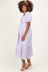 woman wearing a lavender maternity dress with puff sleeves and a tiered skirt, highlighting her baby bump