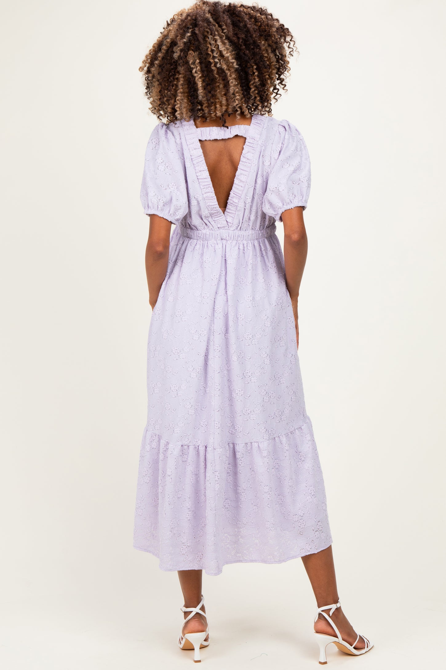 woman wearing a lavender maternity dress with puff sleeves and a back cut-out, showcasing a flowy, tiered design
