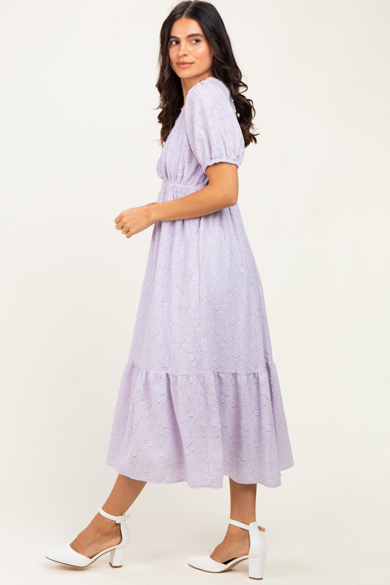 woman wearing a lavender lace midi dress with puff sleeves and a tiered hem, standing sideways