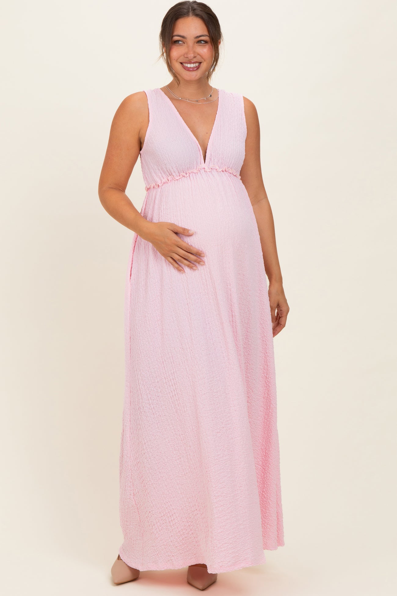 woman wearing a pink maxi maternity dress with a deep V-neck and empire waist, showing her baby bump