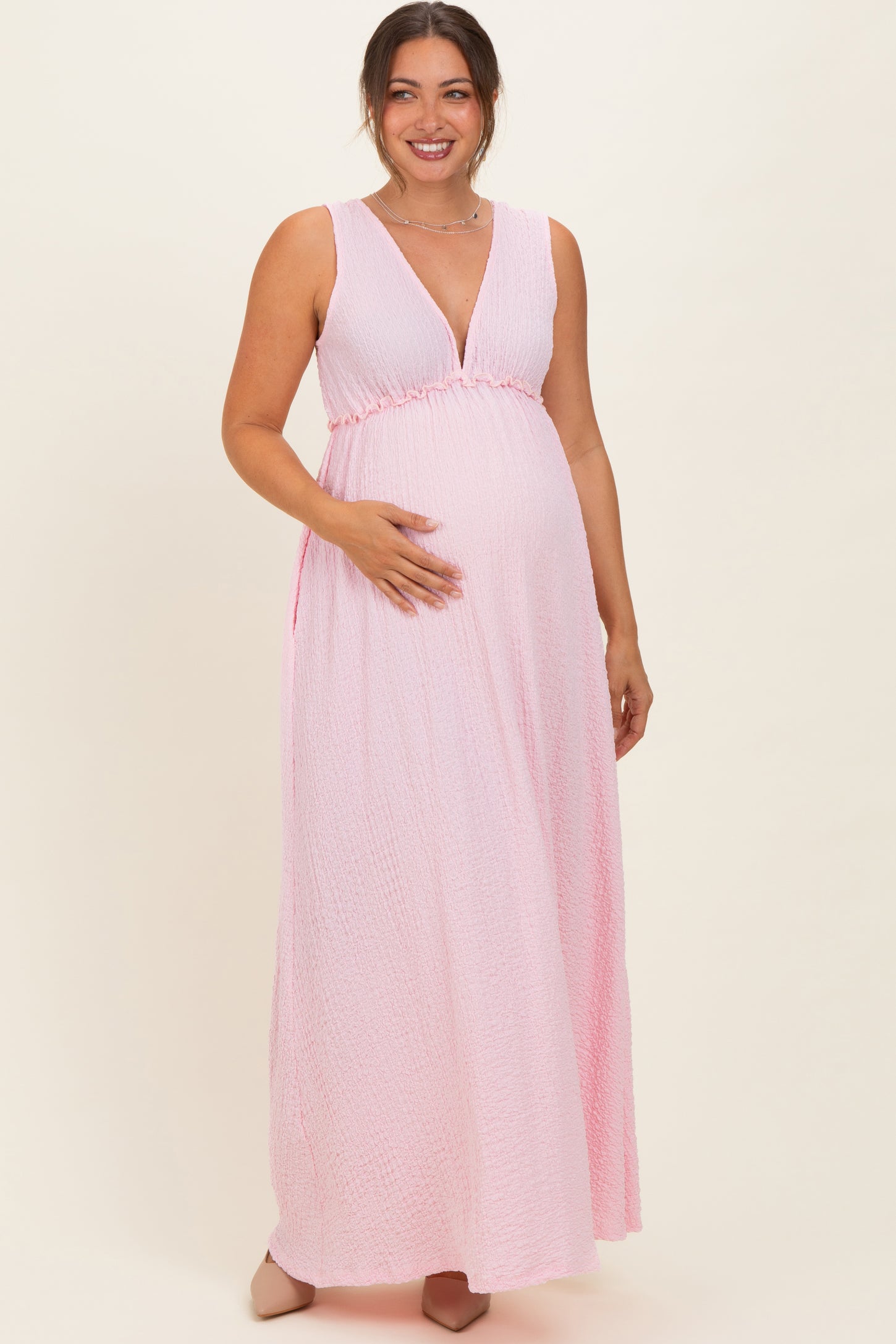 woman wearing a pink maxi maternity dress with a deep V-neck and empire waist, showing her baby bump