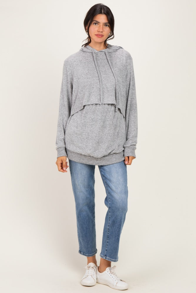 woman wearing a gray cropped hoodie with a layered look and loose blue jeans, standing on a plain background