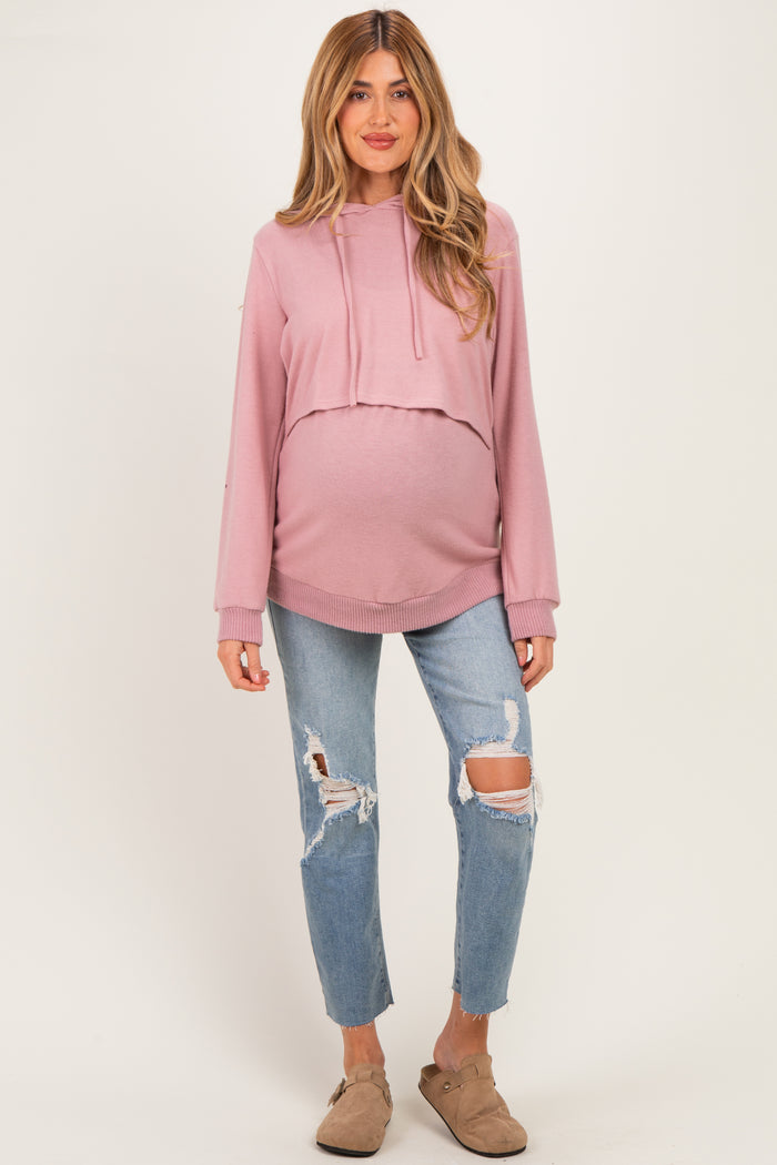 woman wearing a light pink cropped maternity hoodie and distressed blue jeans, showcasing her baby bump