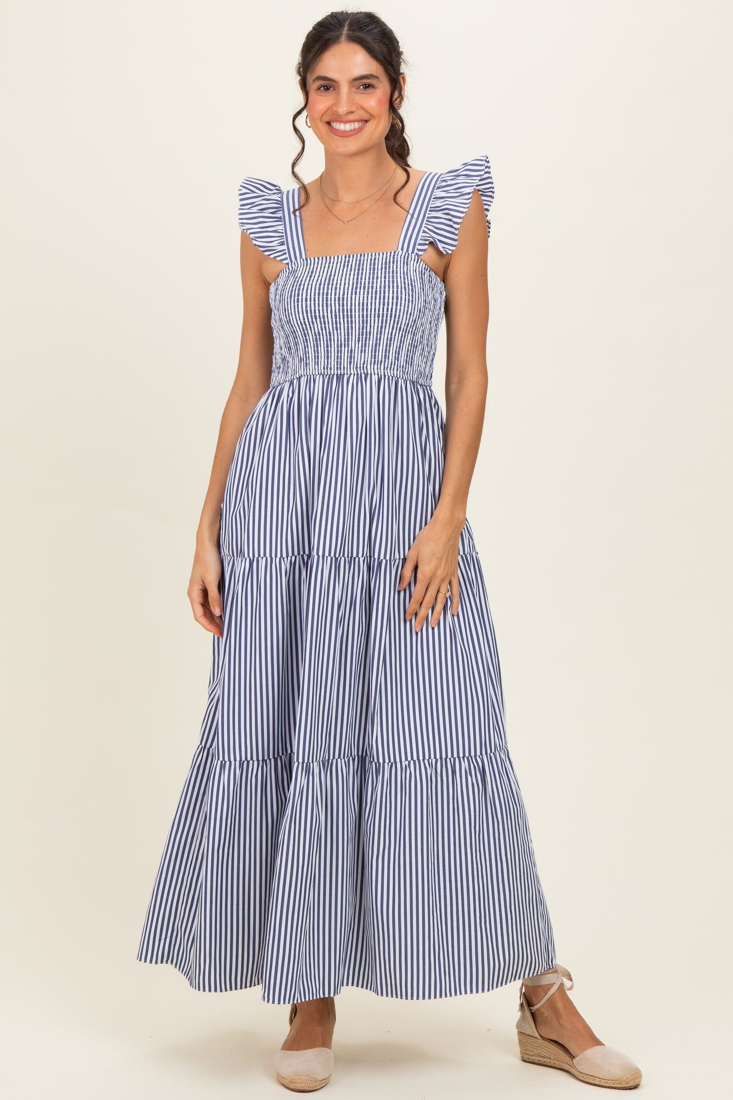 woman wearing a blue and white striped maxi dress with ruffled straps and smocked bodice, standing in a relaxed pose