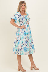 woman wearing a floral print midi dress with blue roses and puff sleeves, styled with heeled sandals