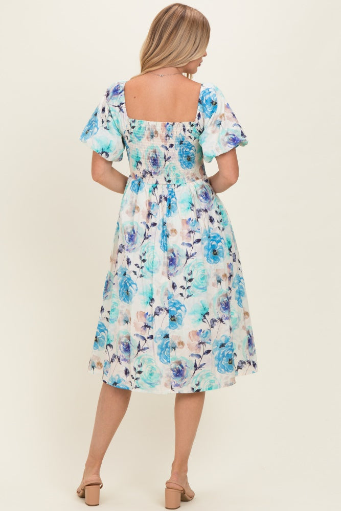 woman wearing a floral midi dress with puff sleeves and a square back design in shades of blue and pastel colors