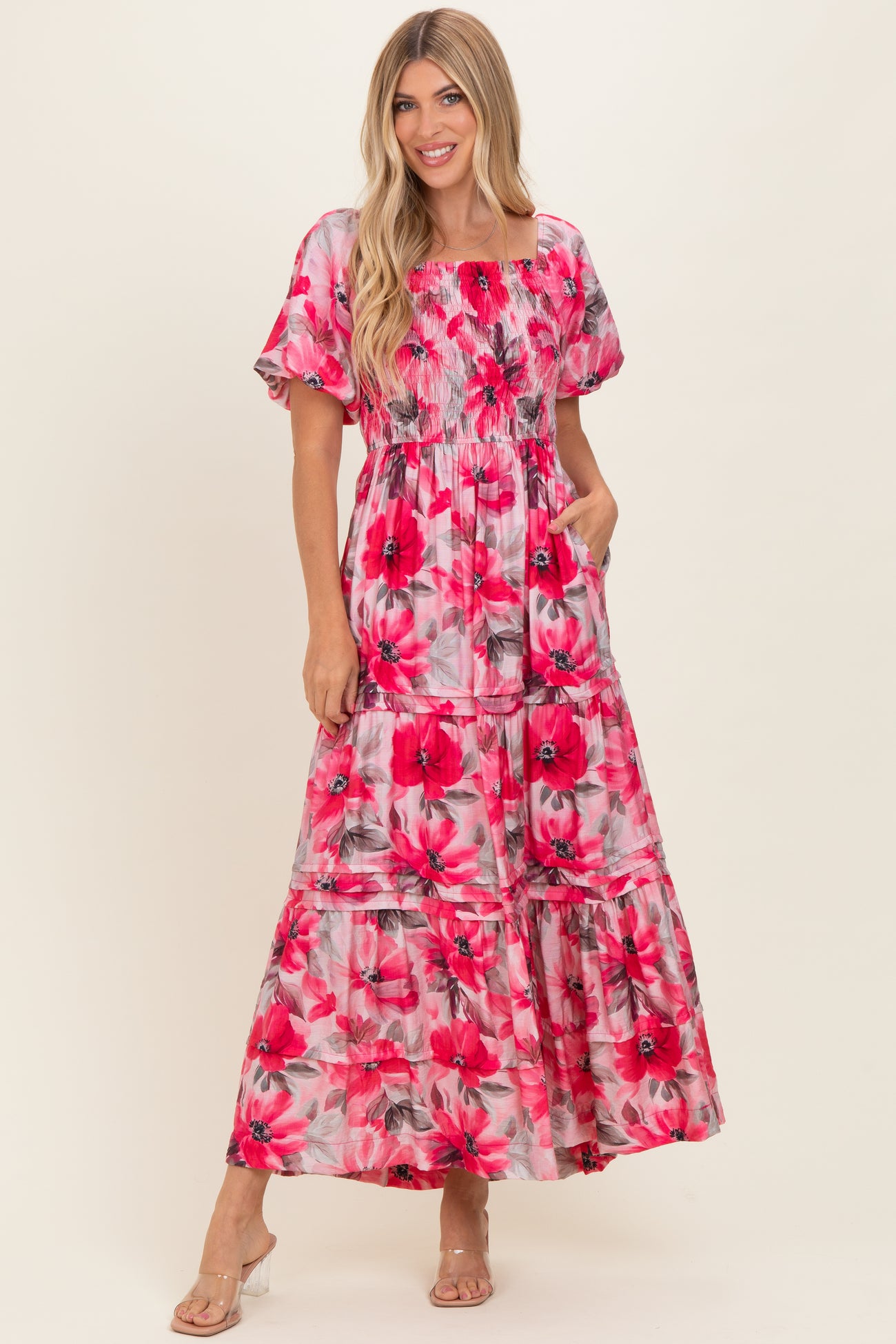 woman wearing a floral pink maxi dress with puff sleeves and pockets, standing and smiling