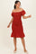 woman wearing a rust red off-the-shoulder knee-length dress with smocked bodice and ruffled hem