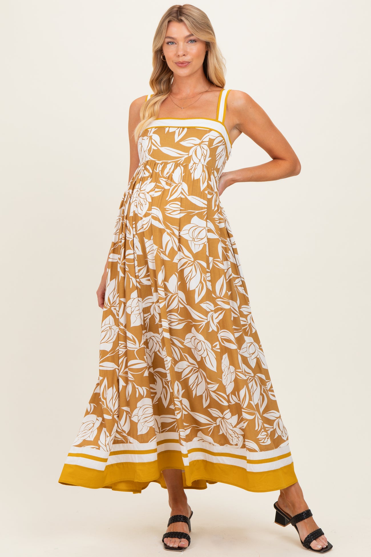 woman wearing a brown floral maternity maxi dress with yellow straps and hem, showcasing her baby bump