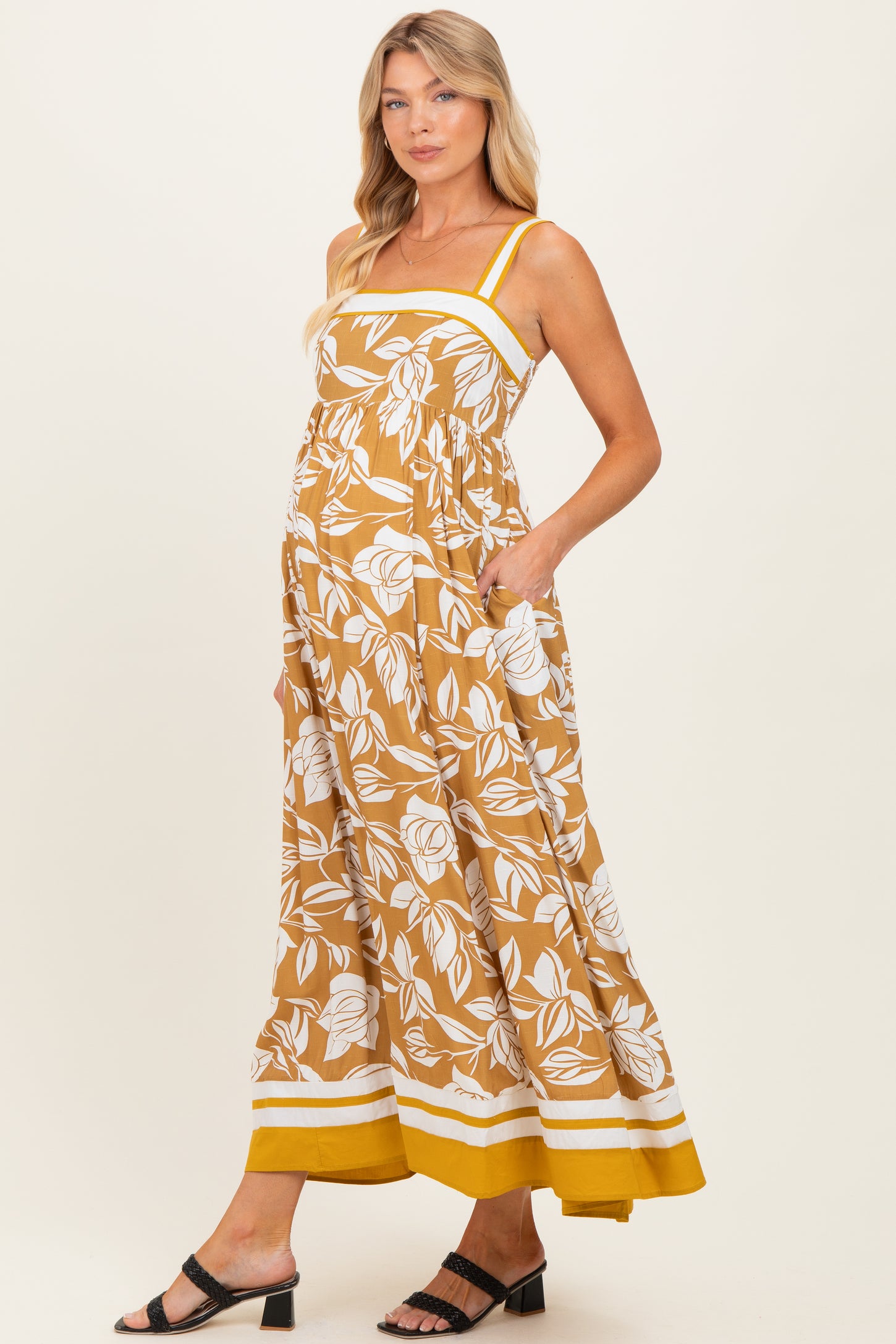 woman wearing a mustard yellow floral print maternity maxi dress with pockets and a baby bump visible
