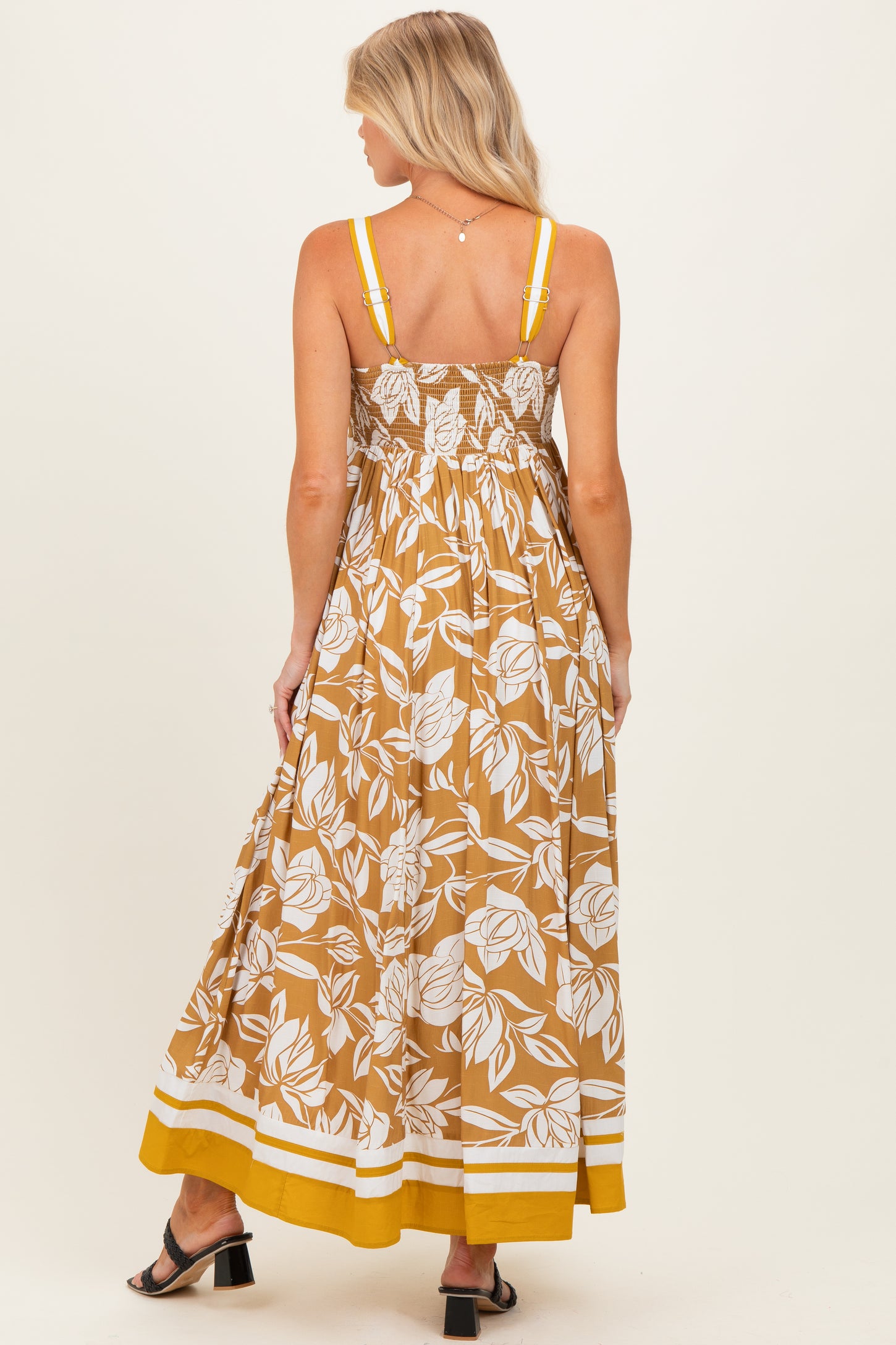 woman wearing a brown floral maternity maxi dress with elastic smocking and yellow accents, showing her back