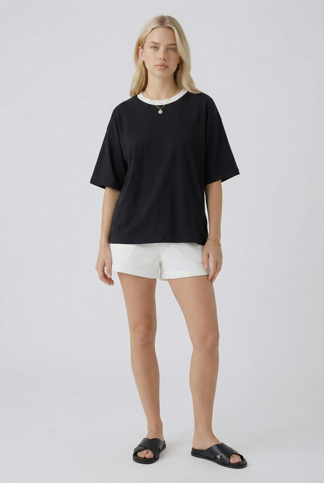 woman wearing a black oversized t-shirt with white trim and white shorts, paired with black slide sandals