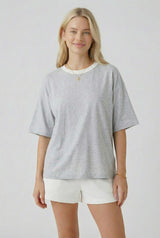 woman wearing a gray oversized t-shirt with a cream trim and white shorts, standing and smiling