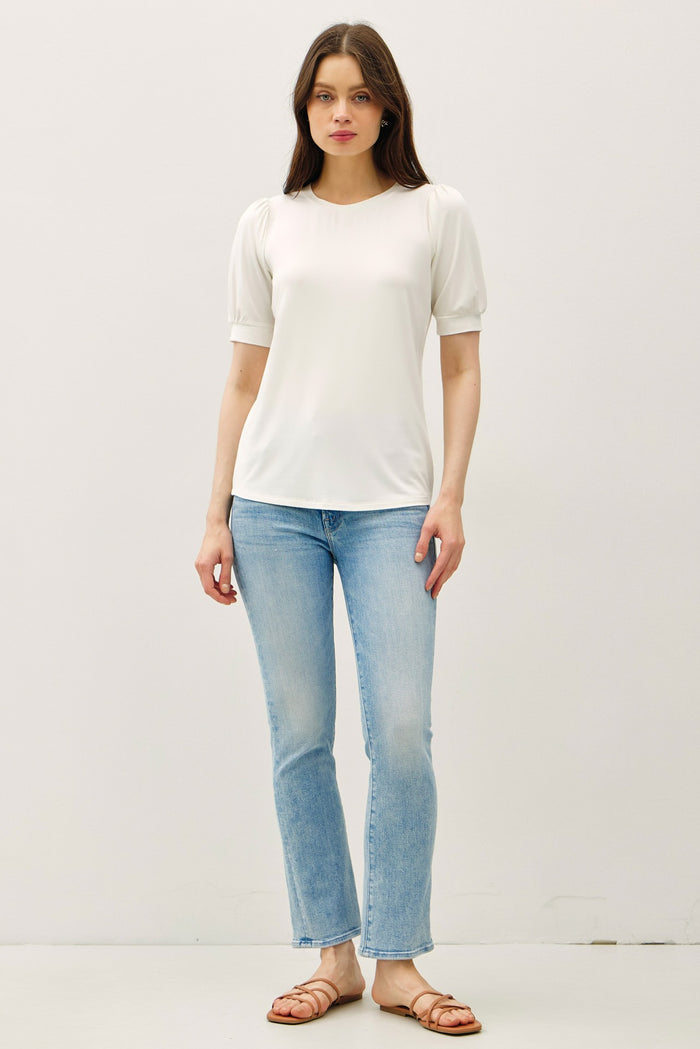 woman wearing a white short sleeve top with puff sleeves and light blue flared jeans