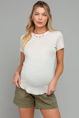 woman wearing a beige short sleeve maternity top and olive green shorts, showing her baby bump