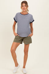 woman wearing a striped maternity top with navy details and olive green shorts, hands in pockets, showing baby bump