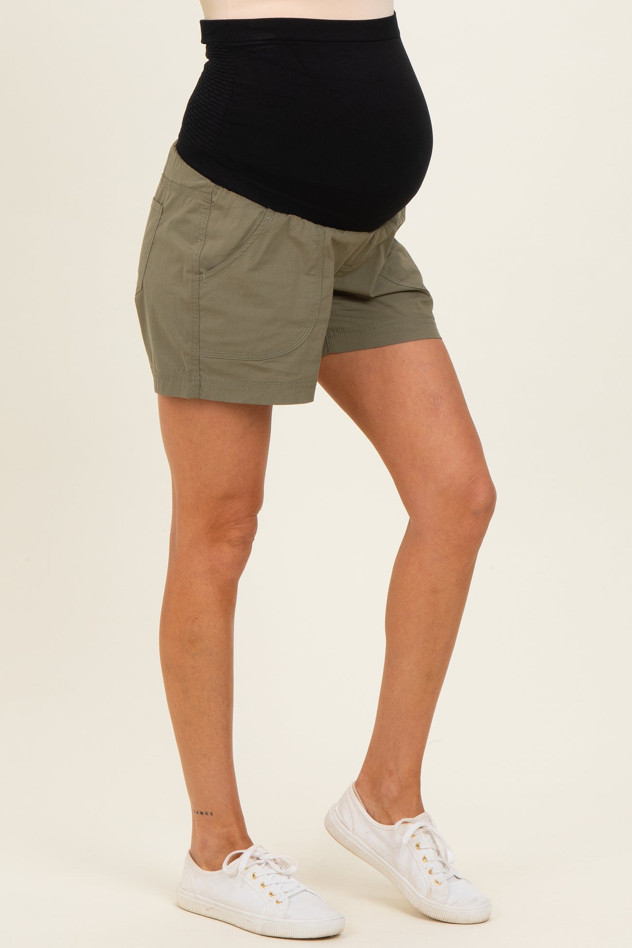 woman wearing olive green maternity shorts and showing her baby bump, paired with white sneakers
