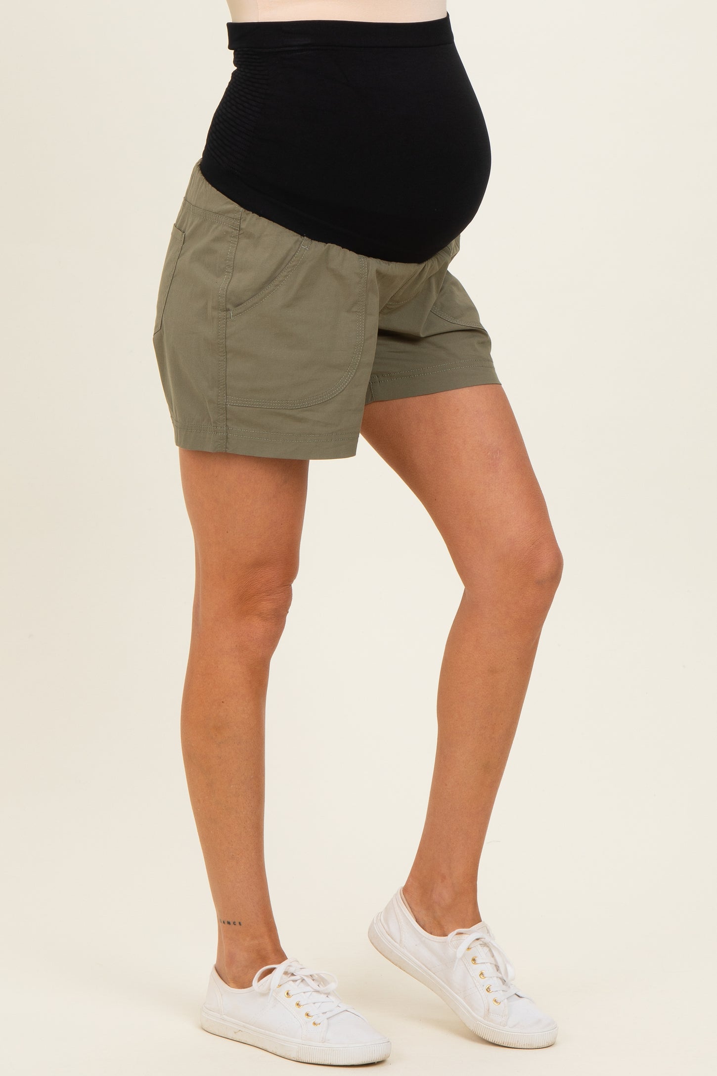 woman wearing olive green maternity shorts and showing her baby bump, paired with white sneakers