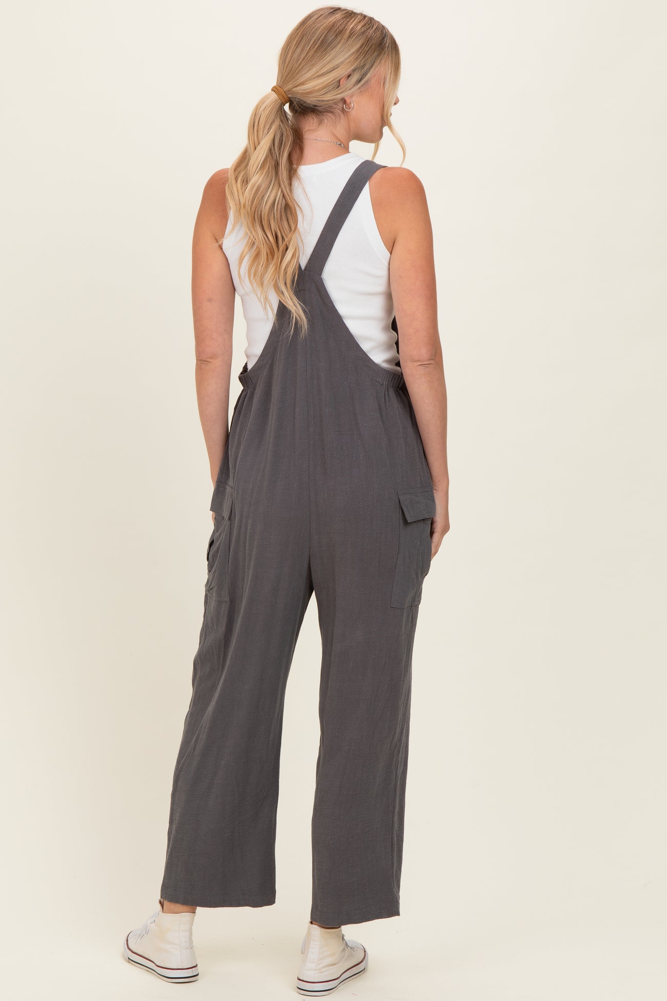 woman wearing a charcoal gray overall jumpsuit with back pockets and a white tank top underneath
