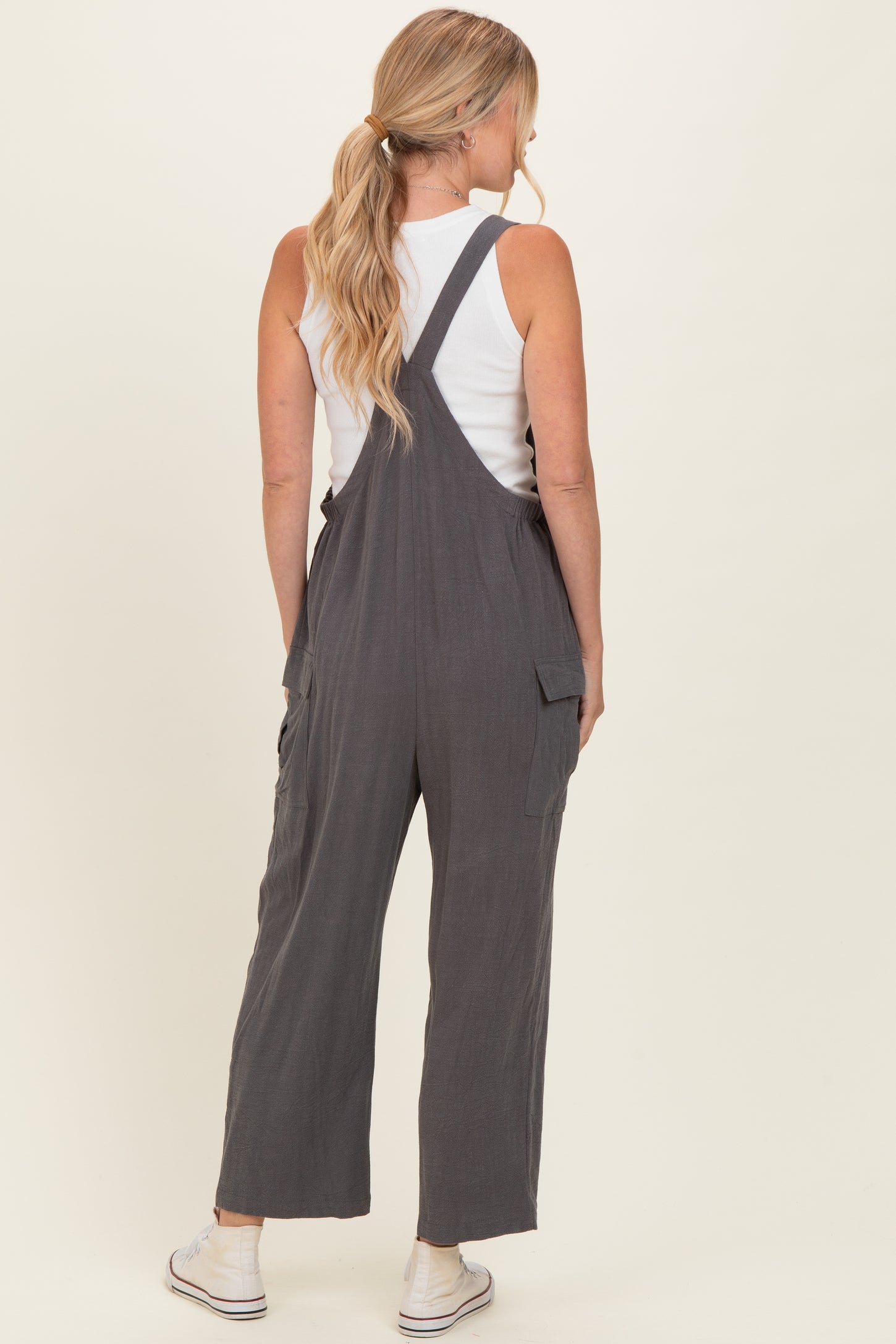 woman wearing a charcoal gray overall jumpsuit with back pockets and a white tank top underneath