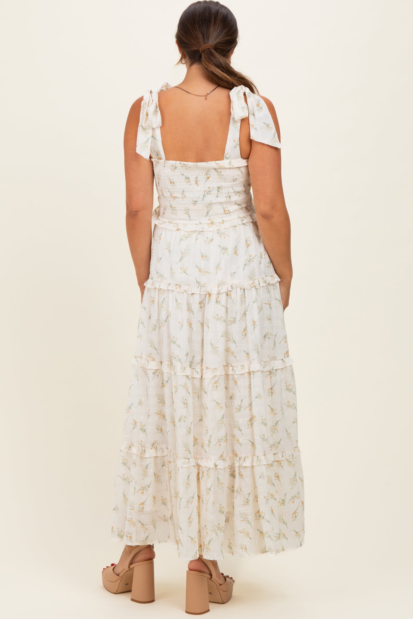 woman wearing a white floral tiered maxi dress with tie straps, showcasing her baby bump from the back
