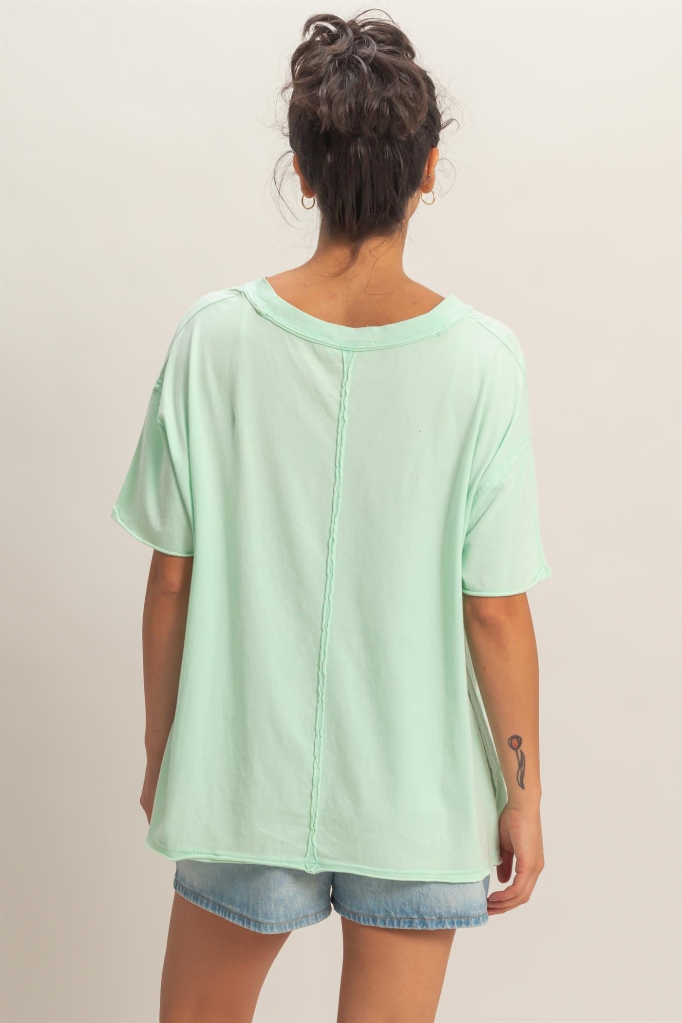 woman wearing a mint green oversized t-shirt, showing the back with a seam detail, styled with denim shorts