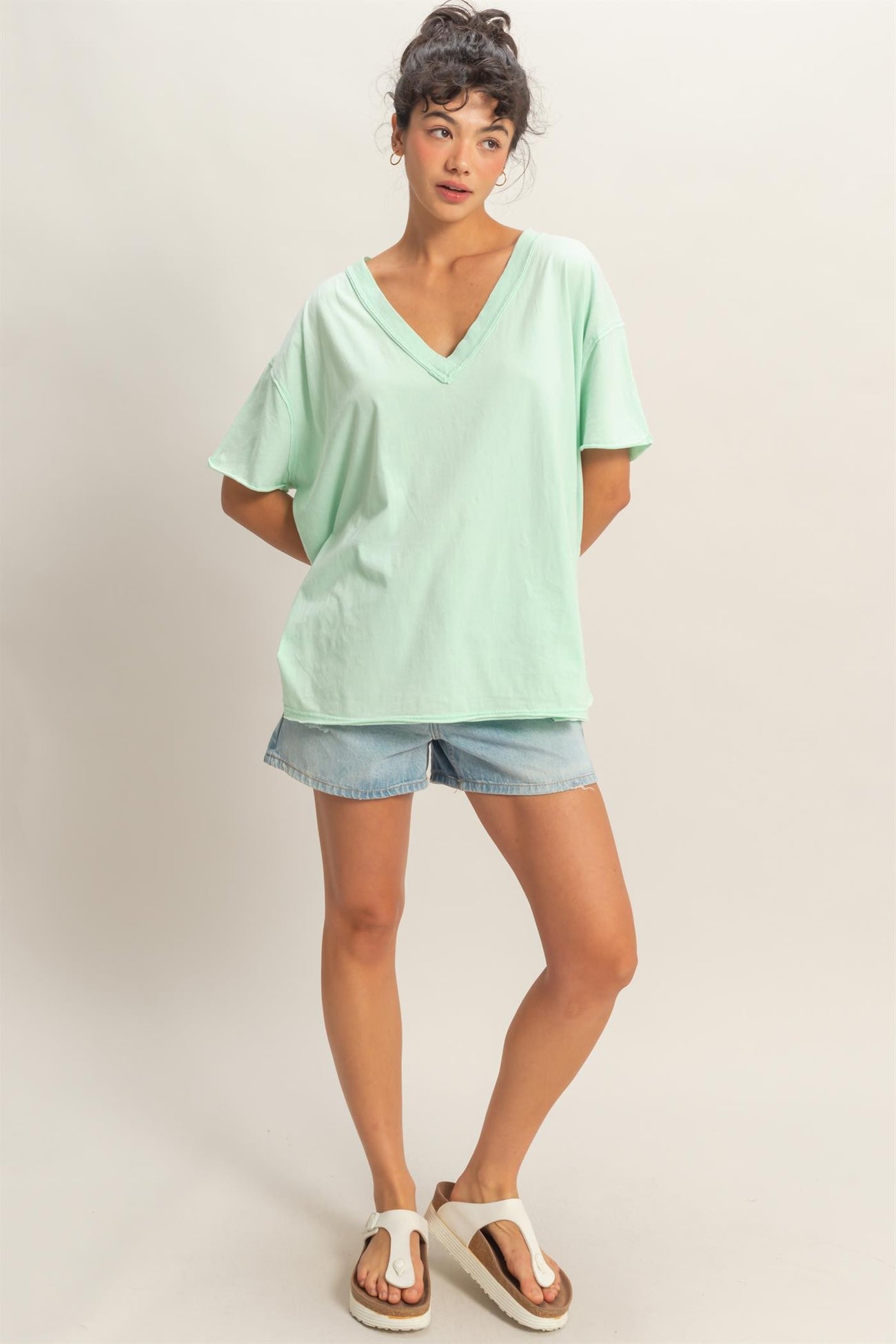 woman wearing a mint green oversized v-neck tee and denim shorts, standing casually with one hand on her hip