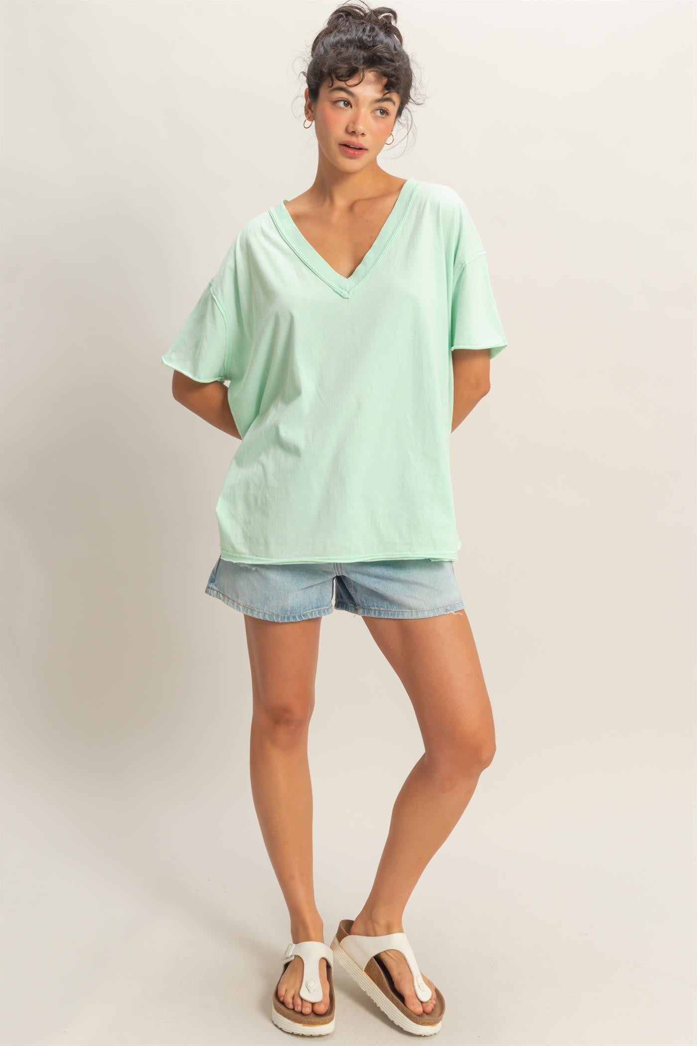 woman wearing a mint green oversized v-neck tee and denim shorts, standing casually with one hand on her hip
