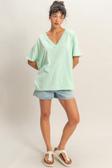 woman wearing a mint green oversized v-neck tee and denim shorts, standing casually with one hand on her hip