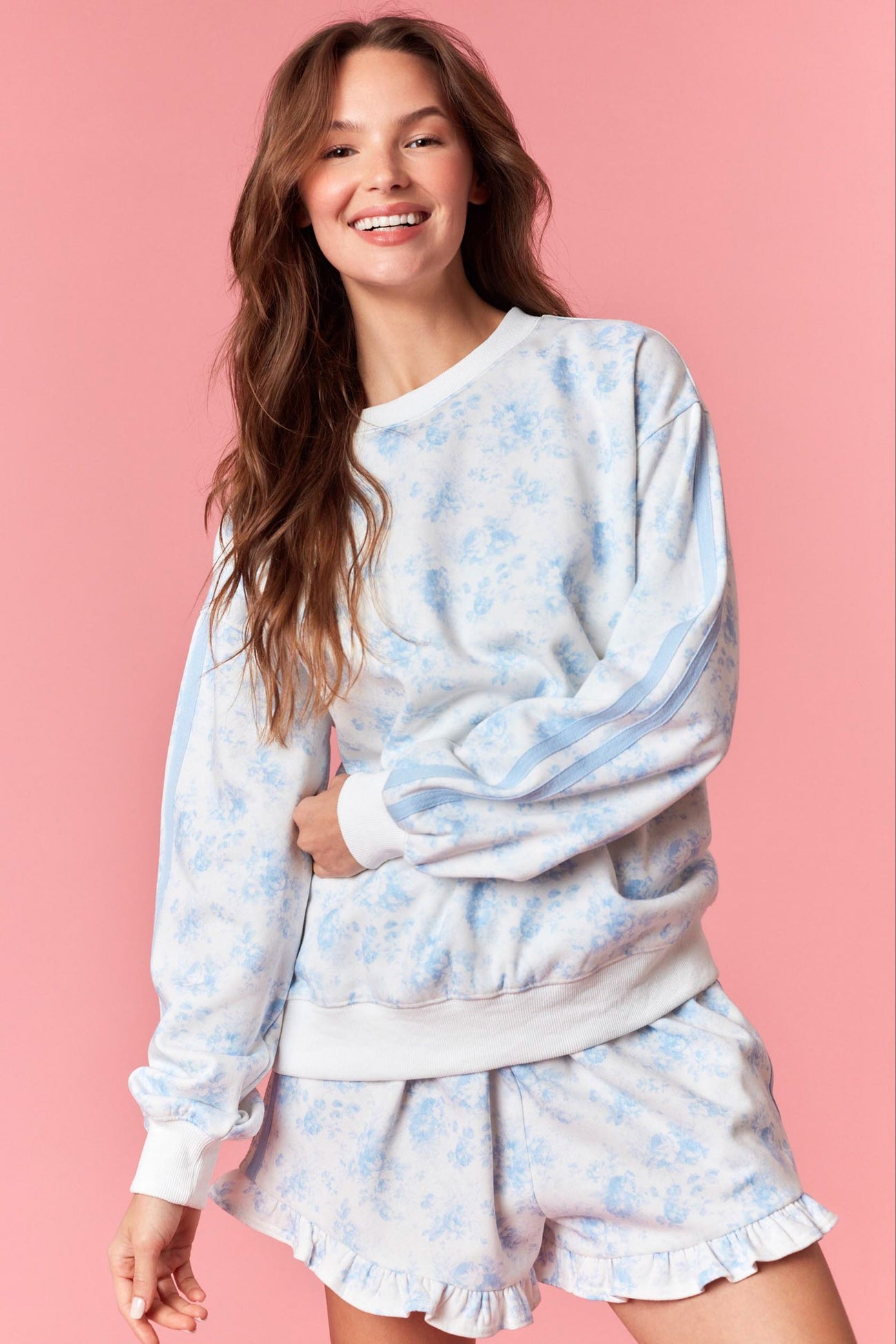 woman wearing a light blue floral print sweatshirt with white stripes and matching ruffled shorts on a pink background