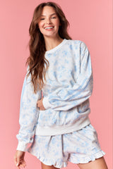 woman wearing a light blue floral print sweatshirt with white stripes and matching ruffled shorts on a pink background