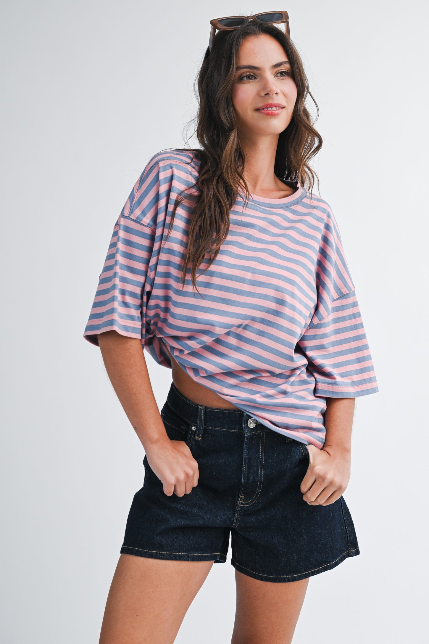 woman wearing a pink and purple striped oversized t-shirt and dark denim shorts, smiling and posing with hands on hips