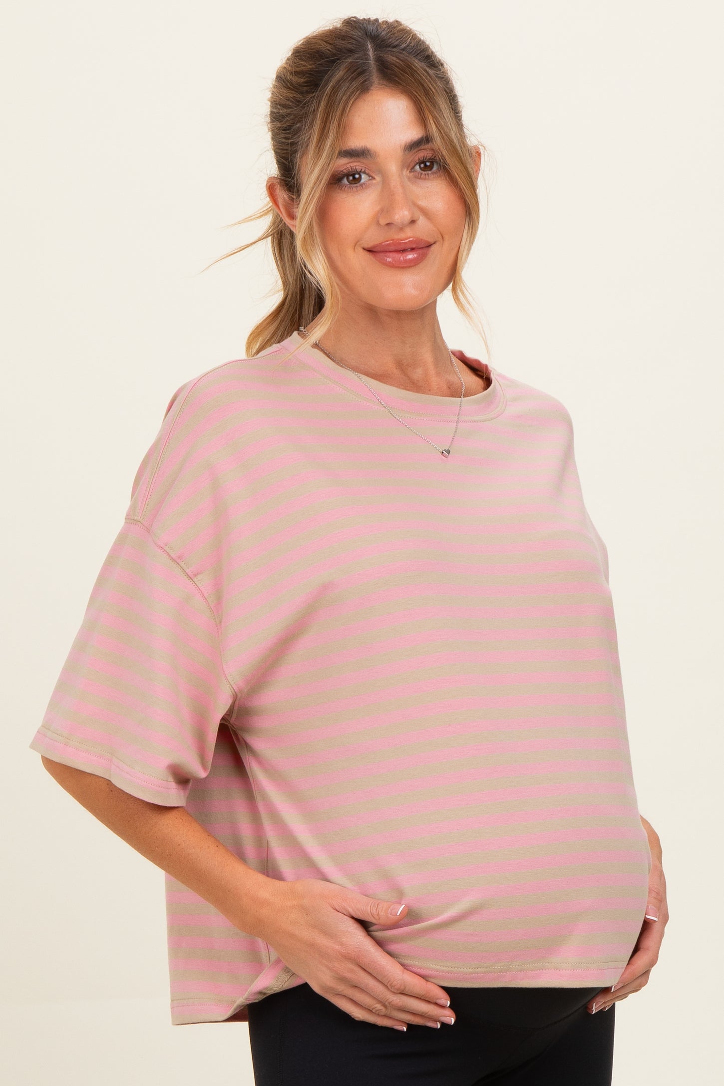 woman wearing a light pink striped maternity top and holding her baby bump