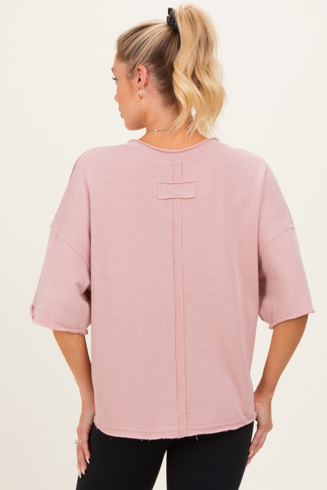 woman wearing a pink oversized maternity top with a relaxed fit and back seam detail