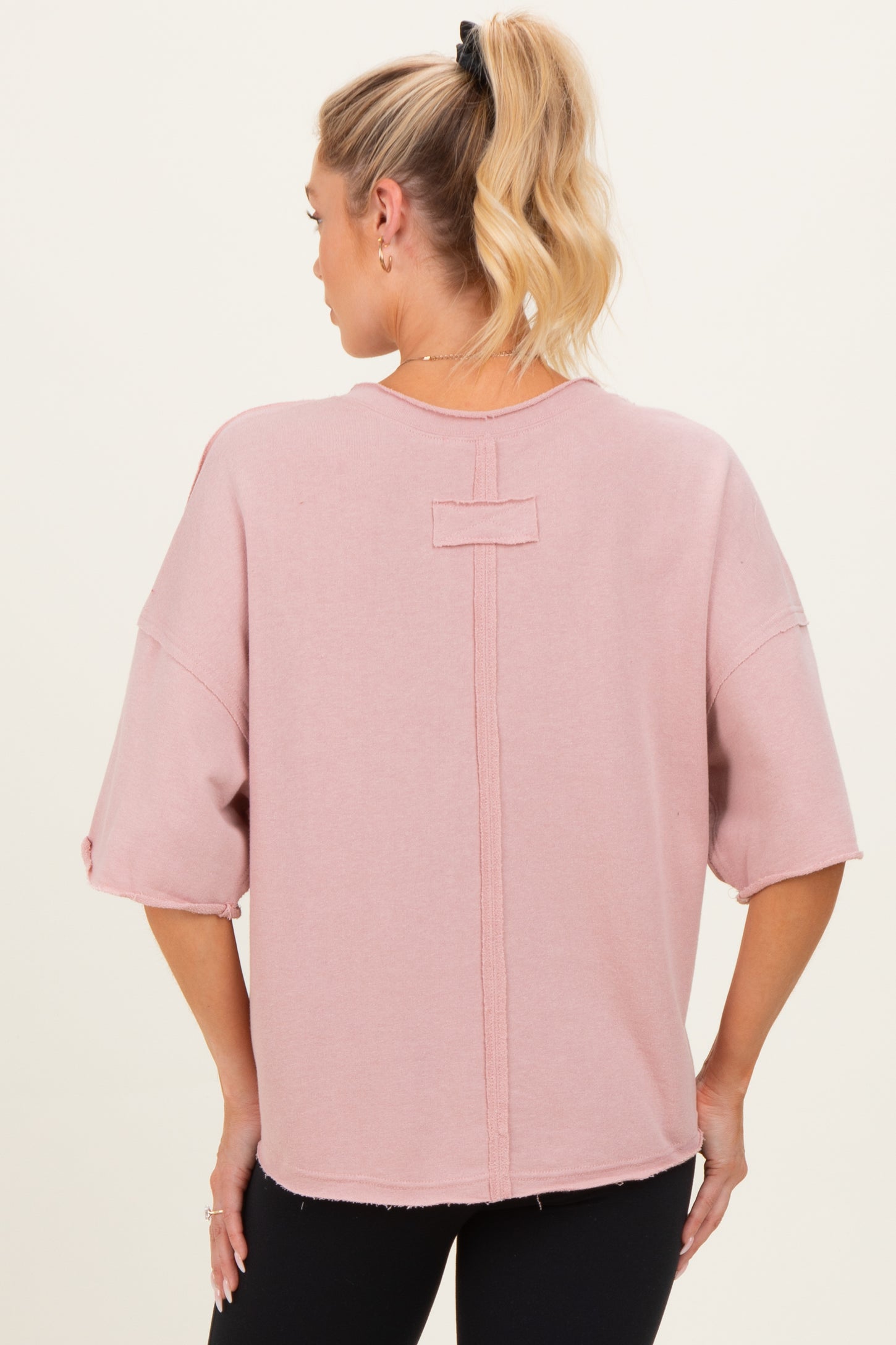 woman wearing a pink oversized maternity top with a relaxed fit and back seam detail