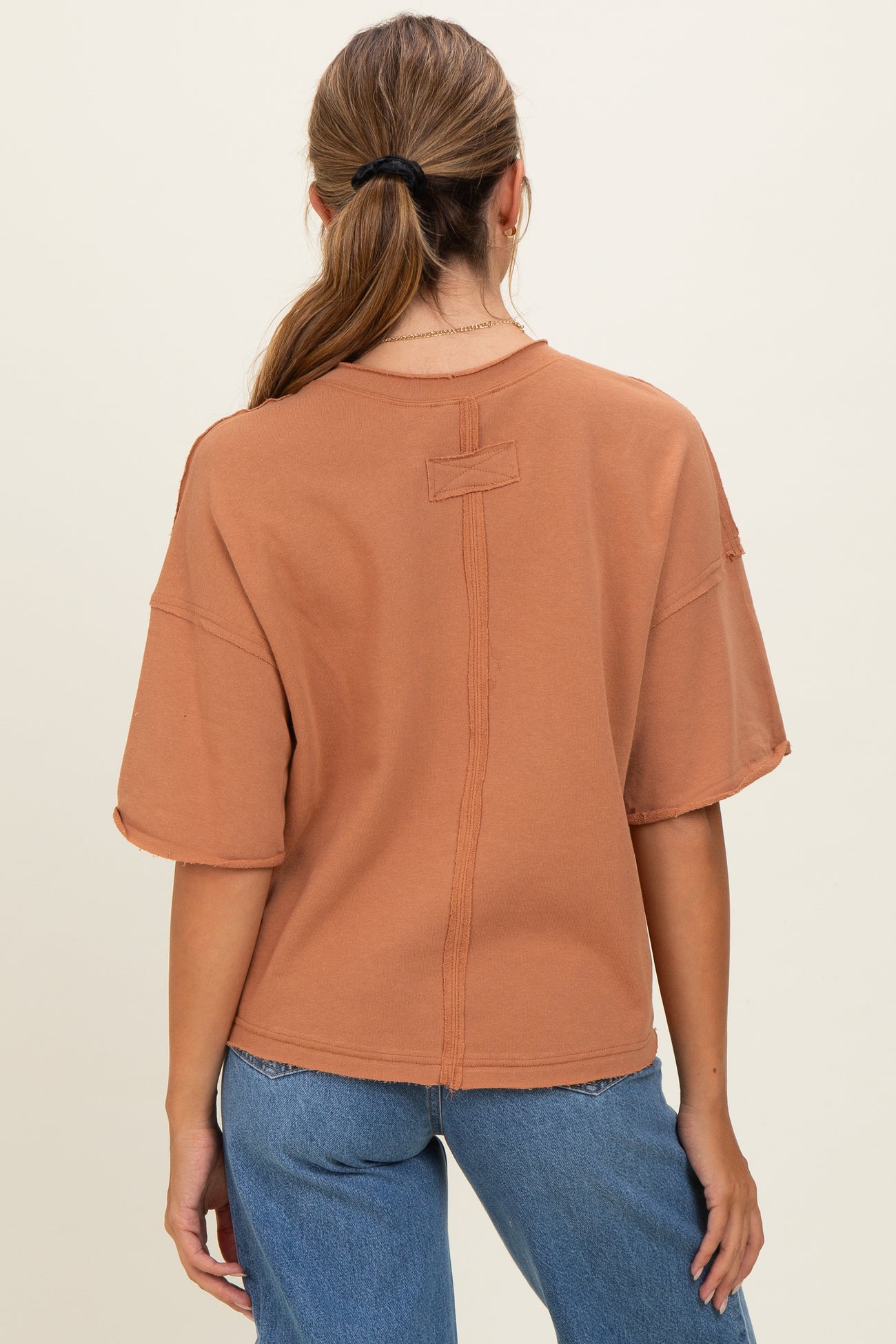 woman wearing a rust-colored oversized t-shirt with short sleeves, showing the back view and relaxed fit