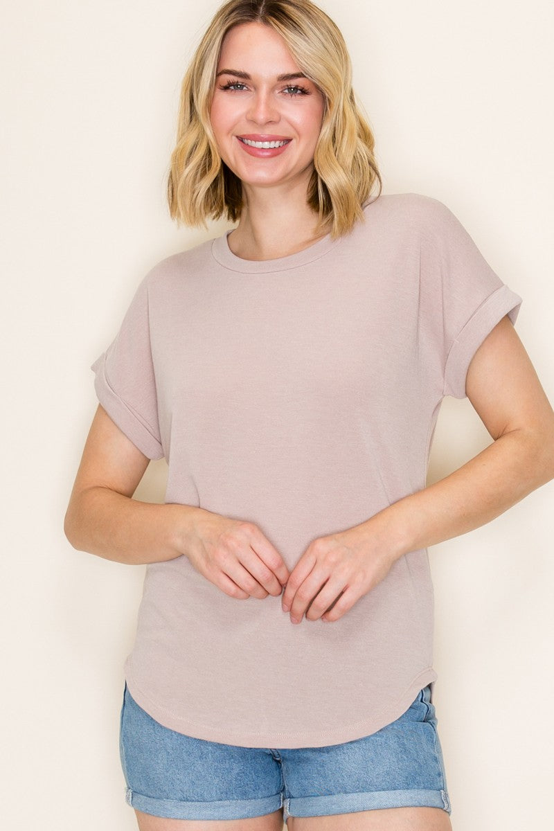 woman wearing a light pink short sleeve top with rolled cuffs and a curved hem, paired with denim shorts