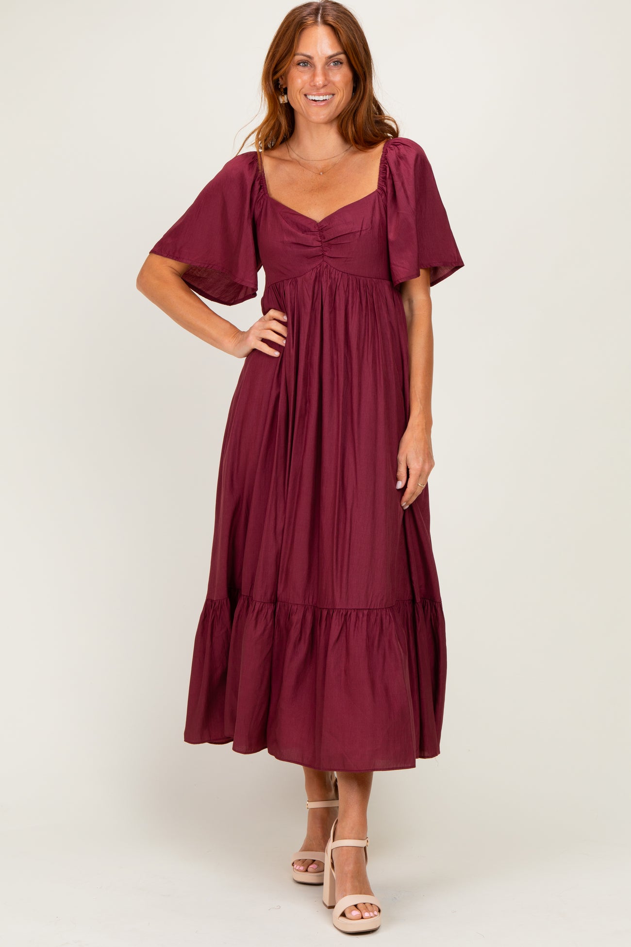 woman wearing a burgundy maxi dress with short sleeves and a tiered skirt, standing with a smile