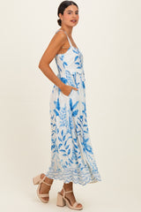 woman wearing a white maxi dress with blue floral patterns and pockets, paired with strappy nude heels