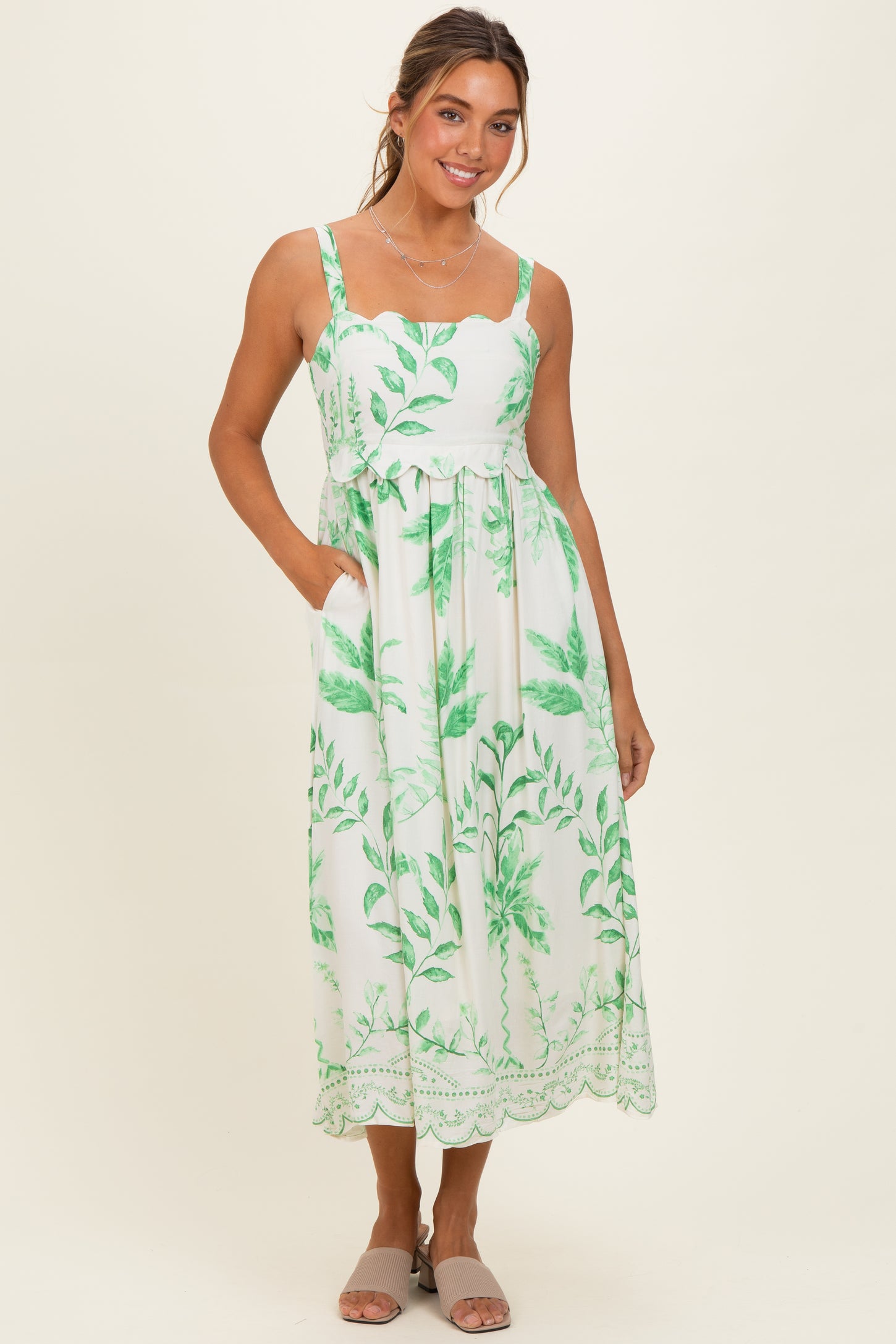 woman wearing a white maxi dress with green leaf print and pockets, styled with a simple necklace and flip flops