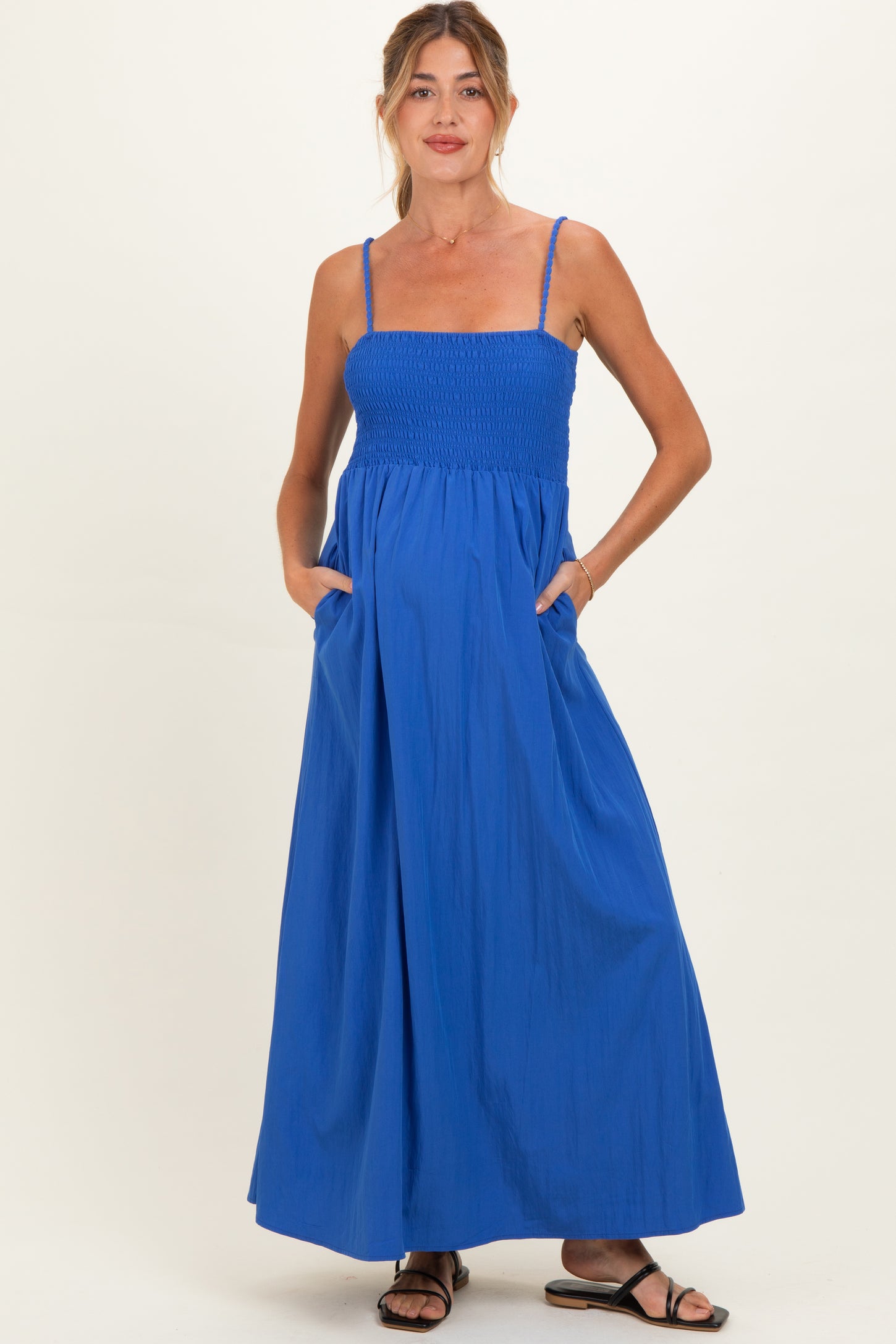 woman wearing a bright blue maternity maxi dress with smocked bodice and pockets, featuring spaghetti straps and a flowing skirt