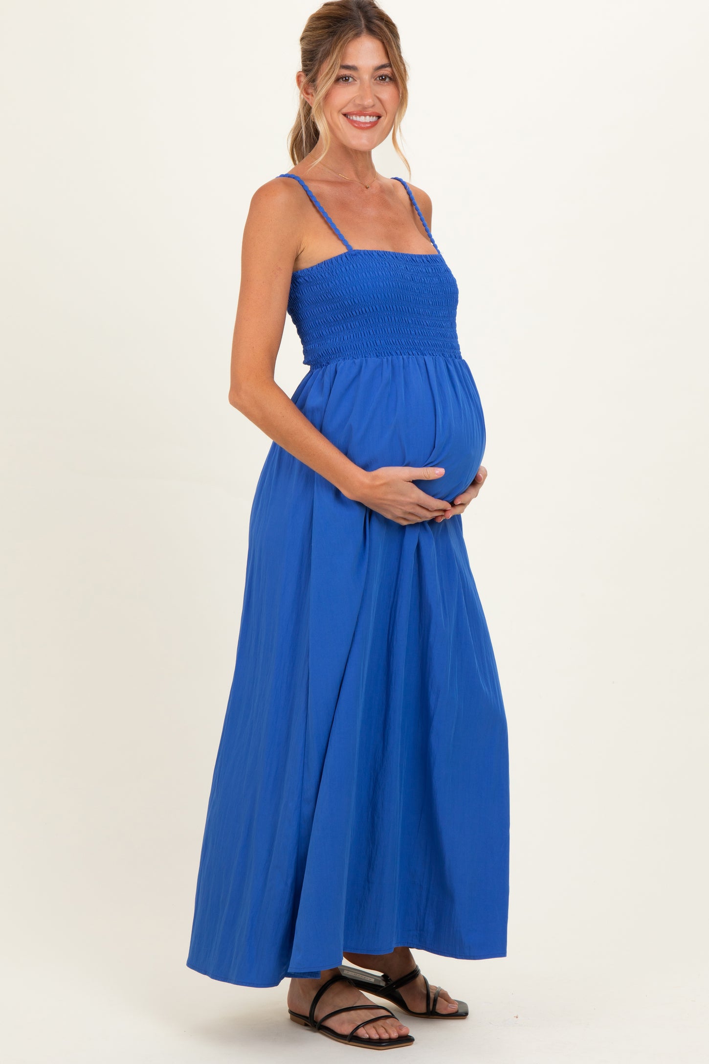 woman wearing a blue smocked maternity maxi dress and holding her baby bump