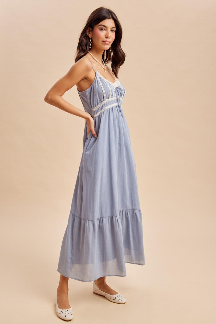 woman wearing a light blue maxi dress with lace details and a ruffled hem, paired with white flats