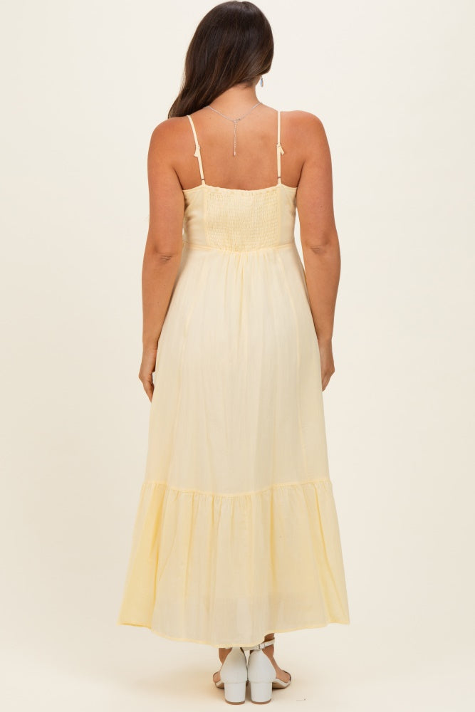 woman wearing a yellow maternity maxi dress with adjustable straps and tiered skirt, showing the back view