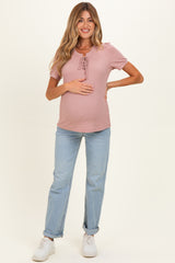 woman wearing a soft pink maternity top with a tie detail, paired with light blue jeans and holding her baby bump
