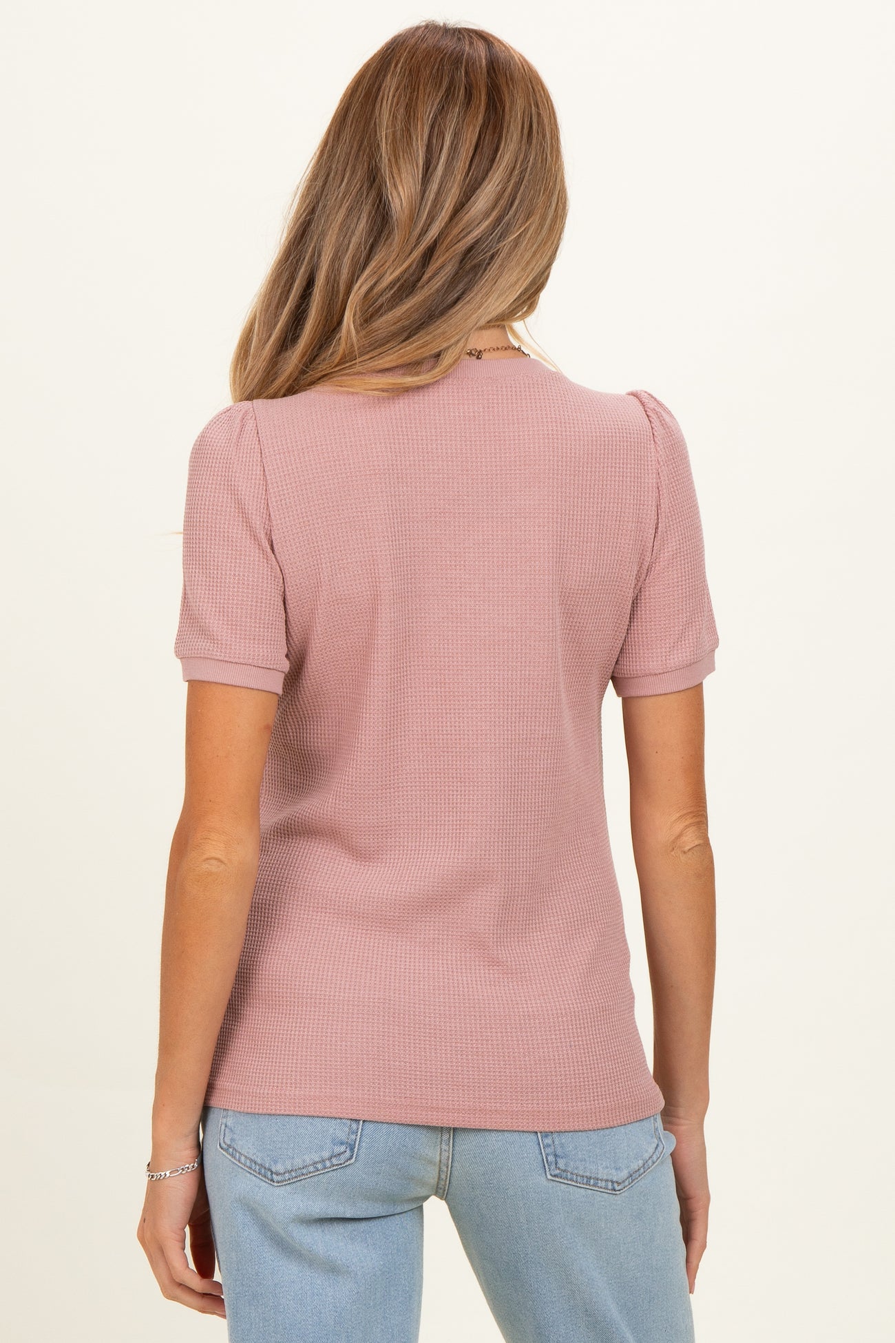 woman wearing a dusty rose short sleeve maternity top with a ribbed texture and a fitted style, seen from the back