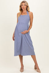 woman wearing a blue and white gingham maternity dress with a fitted bodice and flowy skirt, holding her baby bump